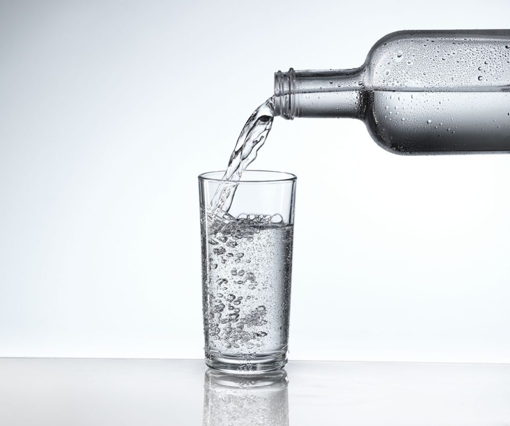 Ein Glas wird mit frischem Eauvation Wasser gefüllt.
